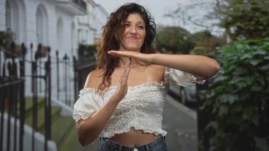 Genç bir İspanyol kadın demir parmaklıkların ve evlerin yakınındaki bir yerleşim yeri caddesinde dururken, mola yeri tabelasını elleriyle imzalar..