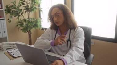 Steteskop tutan kadın doktor dizüstü bilgisayar üzerinde çalışırken çene dinlendiriyor..