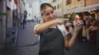 Kot önlüklü ve eldivenli bir kadın çilekli dondurma tutuyor ve caddede onu işaret ediyor..