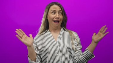 Orta yaşlı bir kadın stüdyo ortamında elleri kaldırıyor, ağzı açık, şaşkınlık içinde..