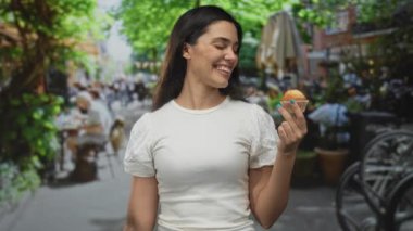 Kalabalık sokak kafesi terasında elinde kek tutarken gülümseyen İspanyol kadın, keyif düşkünlüğü..