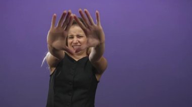 Elleri öne doğru açılmış genç sarışın bir kadın. Avuçları mor stüdyoda görünür durumda. Endişe hassasiyeti var..