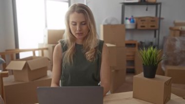 Yeni apartman dairesinde çalışan bir kadın oturma odasında dizüstü bilgisayar kullanarak yeşil ve ışık dekoru elementleriyle hareket ettiğini gösteriyor..