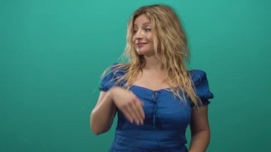 Stüdyoda el hareketleriyle mavi elbise giyen, gülümseyen ve yan bakan, kendine güveni olan bir kadın..