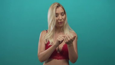 Kırmızı dantelli esmer giyen bir kadın stüdyoda turkuaz duvarla parmak tırnağa dolaşır..