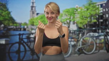 Avuçlarını ovuşturan ve bileklerinde akıllı bir gülümseme, sarışın spor giyim ve sokakta görülebilen bir bisiklet; neşeli bir neşe.