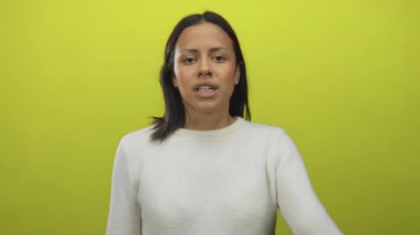 Beyaz kazaklı genç İspanyol kadın, öfke ve yoğunluğu betimleyen parlak sarı bir arka plana karşı güçlü duygular sergiliyor..