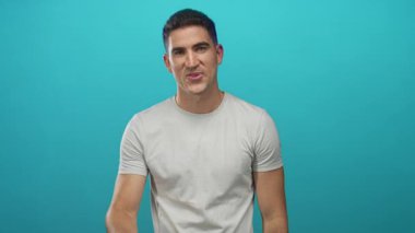 Latin asıllı genç adam turkuaz stüdyoda sağ el işareti gösteriyor..