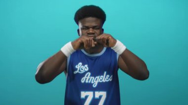 Adam stüdyoda mavi Los Angeles basketbol forması ve beyaz bileklikler giyerek kollarını esnetiyor..