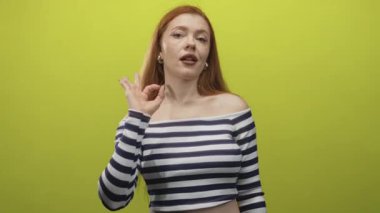 Kızıl saçlı kadın yeşil stüdyoda çıplak omzunu göstererek el hareketi yapıyor..