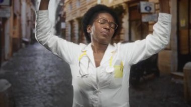 Kadın doktor esniyor, ağzı kapalı, beyaz önlük giyiyor ve kaldırım taşı sokağında steteskop takıyor; yorgunluk tükenmiş..