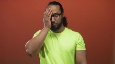 Turuncu stüdyoda, alnına yumruk yemiş, gözlüklü, neon yeşil tişört giyen adam. Yorgun tefekkür..