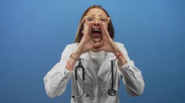 Mavi stüdyoda ellerinde steteskop bardakları olan genç İspanyol kadın doktor eller ağız çevresine; acil halk sağlığı mesajı.