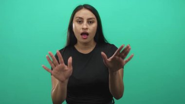 Avuç içleri açık ve elleri havada bir kadın, yeşil bir stüdyo ortamında ağzı açık, kameraya dönük; sürpriz dikkat alarmı..