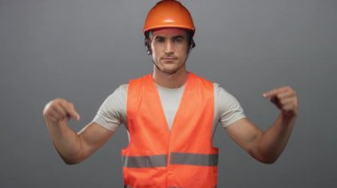 Turuncu şapkalı ve yansıtıcı yelekli genç İspanyol mühendis stüdyoda yeleği işaret ediyor..