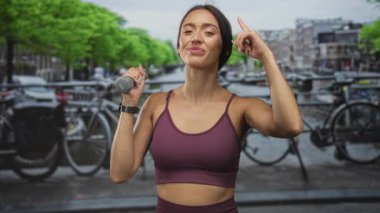 Genç İspanyol kadın Amsterdam caddesinde elinde 1 kg ağırlığında bir dambıl tutarken parmak uçlarına basıyor..