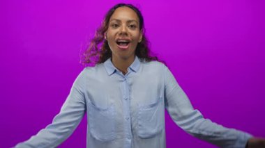 Mor stüdyo arka planında ağzı açık olarak el ele tutuşan kadın, görünür saç hareketi ve alın pozu; sürpriz enerji.