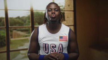 ABD forması giyen bir adam iki parmağını gösterip stüdyoda kameraya doğru öpücük yolluyor..