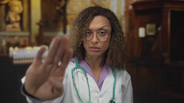 Beyaz laboratuvar önlüğü ve steteskop giyen kadın doktor süslü kilisede durmak için elini kaldırıyor..