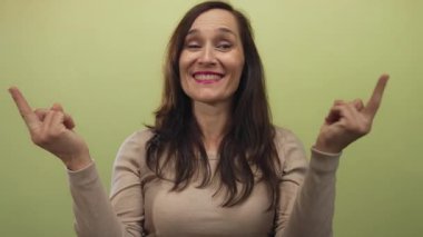 Uzun düz saçlı, Latin kökenli genç bir kadın stüdyoda gülümserken orta parmaklarını sergiliyor..