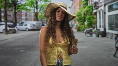 Güneşli bir sokakta elinde dondurma tutan İspanyol kadın dükkan önü ve bisikletlerle göğüs göğüse; memnuniyet yazı.