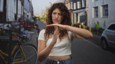 Elleri havada bir kadın park halindeki bisiklet ve arabanın yakınındaki sokakta jest yapıyor, gergin ifade ve odaklı duruş; iddia sınır hüsranı.