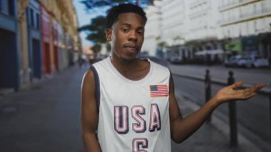 Kolsuz Amerikan basketbol forması giyen Afro-Amerikan bir adam şehir caddesinde avucunu yana doğru uzatıyor..