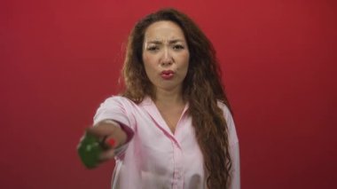 Stüdyoda elini öne uzatan genç bir kadın kırmızı arka planda, pembe gömlek giyiyor; hayal kırıklığı talebi.