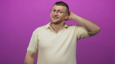 Stüdyoda eli arkada gülümseyen bir adam mor arka planda krem rengi polo ve gözlük takıyor..