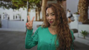 Güneşli bir sokakta beyaz bina cephelerine el ve kırmızı tırnaklarla barış işareti gösteren bir kadın..