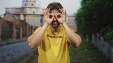 Sarı tişörtlü genç bir adam tarihi bina cephelerinin yakınındaki eski bir kasabanın parke taşı sokağında elleri üzerinde dürbün yapıyor..