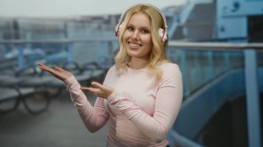 Bir yolcu gemisinde gülümseyen, kulaklık takan genç, sarışın bir kadın heyecanlı bir seyahat ve rahatlama ortamında heyecanını sergiliyor.