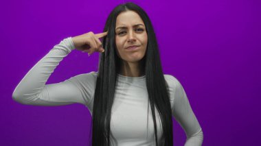 Beyaz gömlekli İspanyol kadın, canlı mor arka plana karşı çılgınca jest yapıyor. Duygularını ve ifadelerini minimalist bir ortamda sergiliyor..