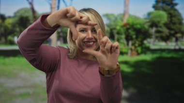 Ormanda güneşli ağaç tepe örtüsünün altında gülümserken kadın yüzünü parmaklarıyla çerçeveler; hayal gücü.