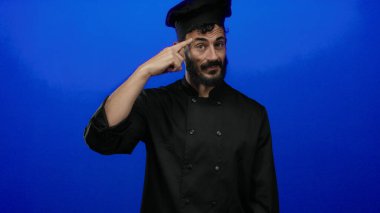 Siyah şef üniformalı İspanyol bir adam sakallı, parlak mavi bir arka plana karşı düşünceli, profesyonel bir yemek pişirme havası yayıyor..