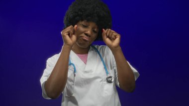Mavi stüdyoda steteskop takan genç Afrikalı Amerikalı kadın doktor, hüzün yorgunluğu..