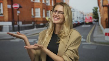 Canlı bir şehir caddesinde elleri açık sunan, şık bir bej ceket giyen, sarı saçlı, gülümseyen yüzünde gözlüklü, kentli yaşam tarzını ve enerjisini gösteren bir kadın..