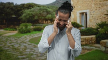 Taş avluda ağaçlarla çevrili bir avluda diş ağrısı için el üstünde akıllı telefonu kulağına tutan adam endişeleniyor..