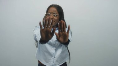 Avuç içleri açık, gözlüklü ve açık mavi düğmeli gömlekli bir kadın stüdyoda görülüyor..