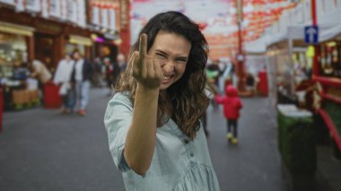 Kot giyen genç İspanyol kadın sırıtıyor ve kalabalık caddede orta parmağını gösteriyor..