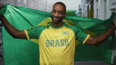 Brezilya bayrağı tutan ve sarı Brezilya forması giyen bir adam, bir şehir caddesinde kollarını açarak gülümseyerek takımını desteklerken; vatansever gururu.