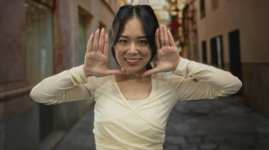 Kadın gülümsüyor ve elleri ile bir çerçeve yapıyor tarihi bir kasaba ortamında ayakta dururken, eski bir Çin caddesinde neşeli bir yüz ifadesi yakalıyor..