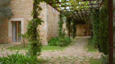 Yeşillik ve ahşap çardaklarla çevrili taştan bir yolu olan eski bir Akdeniz evinin bulanık görüntüsü sakin ve sakin bir açık hava ortamı yaratıyor..