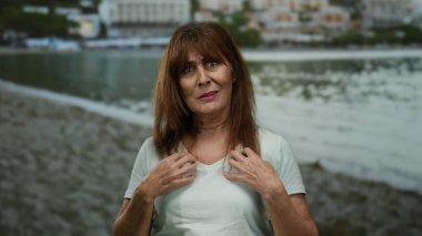 İspanyol kıdemli kadın deniz kenarında ve arka planda binalar olan bir sahilde sürpriz yapıyor..