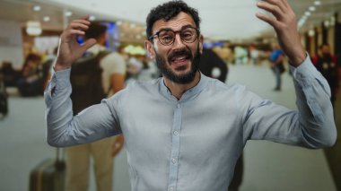 Sakallı İspanyol bir adam alışveriş merkezinin arka planında heyecanlı bir şekilde bağırıyor. İnsanlar enerjik bir şekilde hareket ediyor..