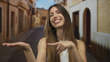 Genç İspanyol kadın gülümseyen parmaklarını açık avucuna işaret ediyor güneşli eski bir kasaba caddesinde; mutluluğu vurgula.