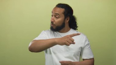 Açık yeşil stüdyoda, uzanmış kollu ve dışa dönük yüzlü bir adam, dikkat çeken ve sağlam konuşan bir jest ortası; suçlayıcı..