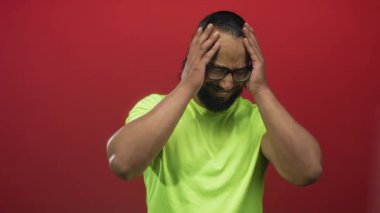 Kırmızı stüdyoda yüzü asık, gözleri kapalı, neon yeşil gömlek giyen bir adam hayal kırıklığı baş ağrısı..