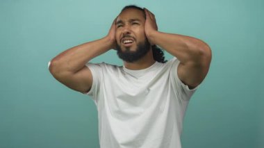 Beyaz tişört ve sakal giyen, el pençe divan duran ve deniz mavisi stüdyoda kederli yüzle el ele tutuşan bir adam; gürültü bunalımı.