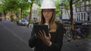 Şehir caddesinde bisikletli ve arabalı bir tableti tutan ve tıkırdatan kadın mühendis; profesyonel planlama güveni.